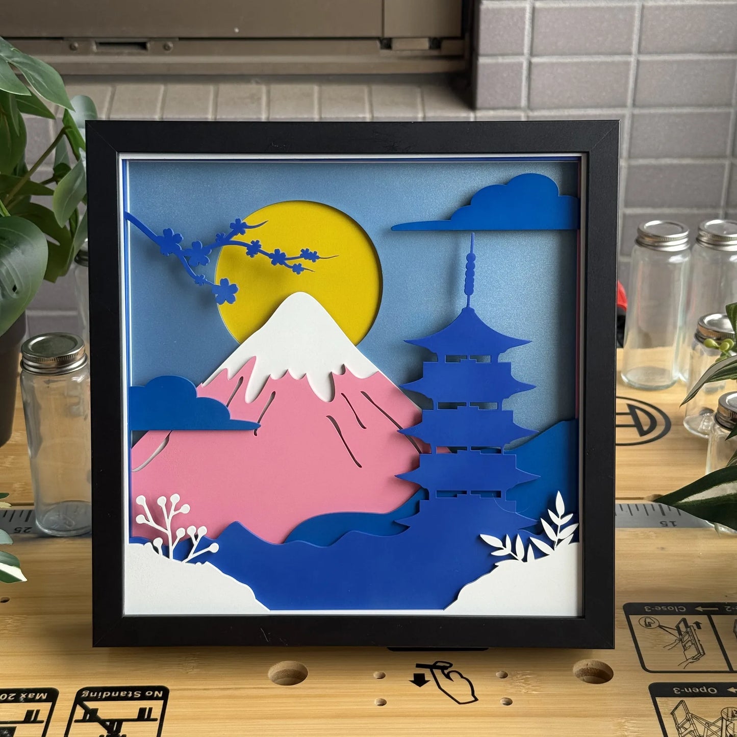 Framed artwork with Mount Fuji and a pagoda on a wooden surface.
