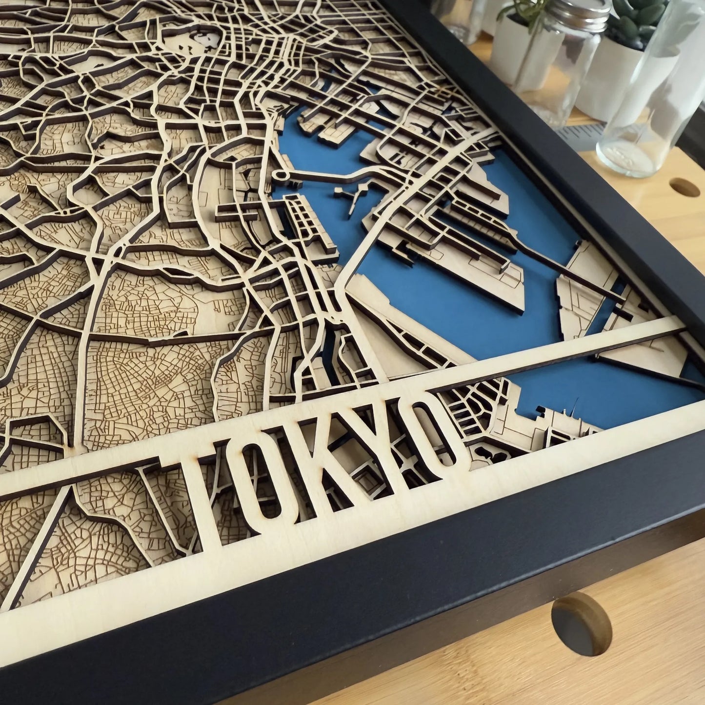 Wooden laser-cut map of Tokyo with blue highlighting on a wooden surface.